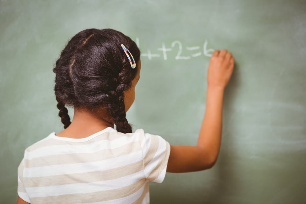 Rear view of little girl writing on blackboard in the classroom